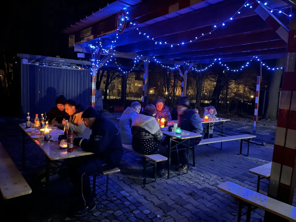 Leute sitzen an Biertischen beim essen, Dekoration mit blauen Lichterketten